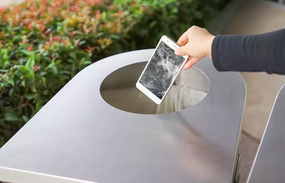 Hand dropping a broken cellphone in the trash